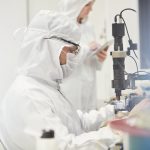 Workers In Protective Suits Using Machinery In Fiber Optics Research And Testing Laboratory